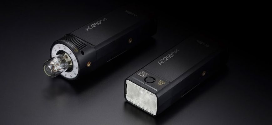 Два акумуляторні спалахи Godox AD200Pro II лежать на темному столі: зліва — з головкою H200J II та відкритою лампою для великих модифікаторів, справа — з класичною прямокутною лінзою Френеля H200 II